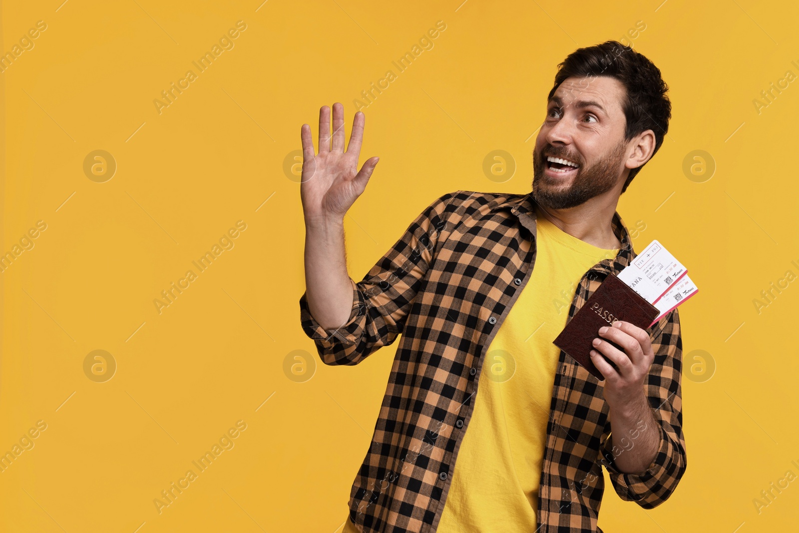 Photo of Smiling man with passport and tickets waving hello on yellow background. Space for text