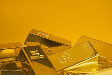 Many shiny gold bars on orange background, closeup. Space for text