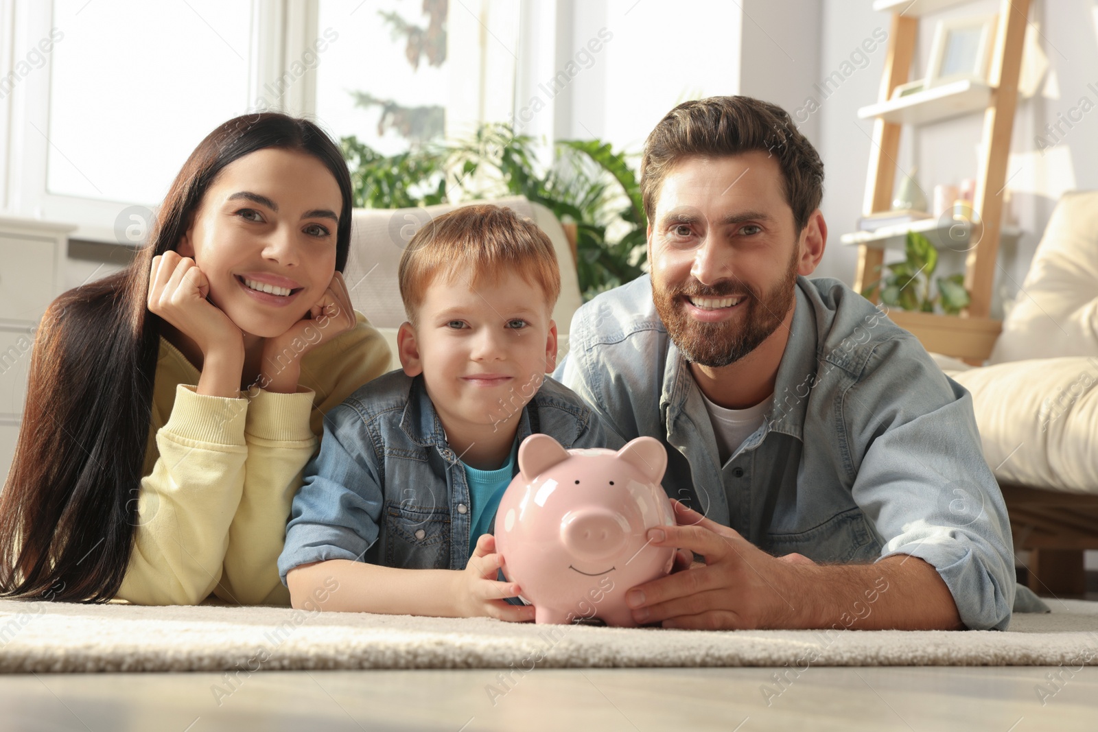 Photo of Happy family with ceramic piggy bank on floor at home
