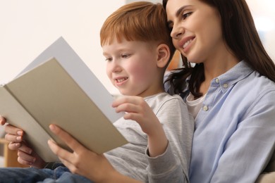 Photo of Happy mother reading book with her child at home, closeup