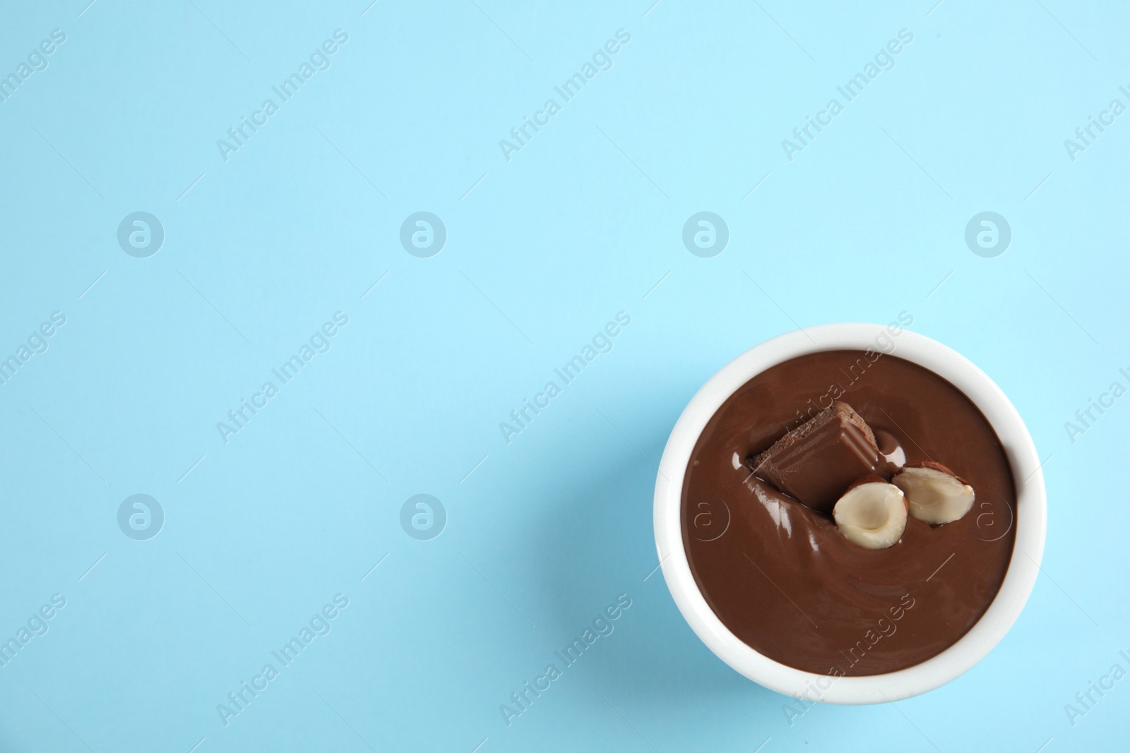 Photo of Bowl with sweet chocolate cream and hazelnuts on color background, top view. Space for text