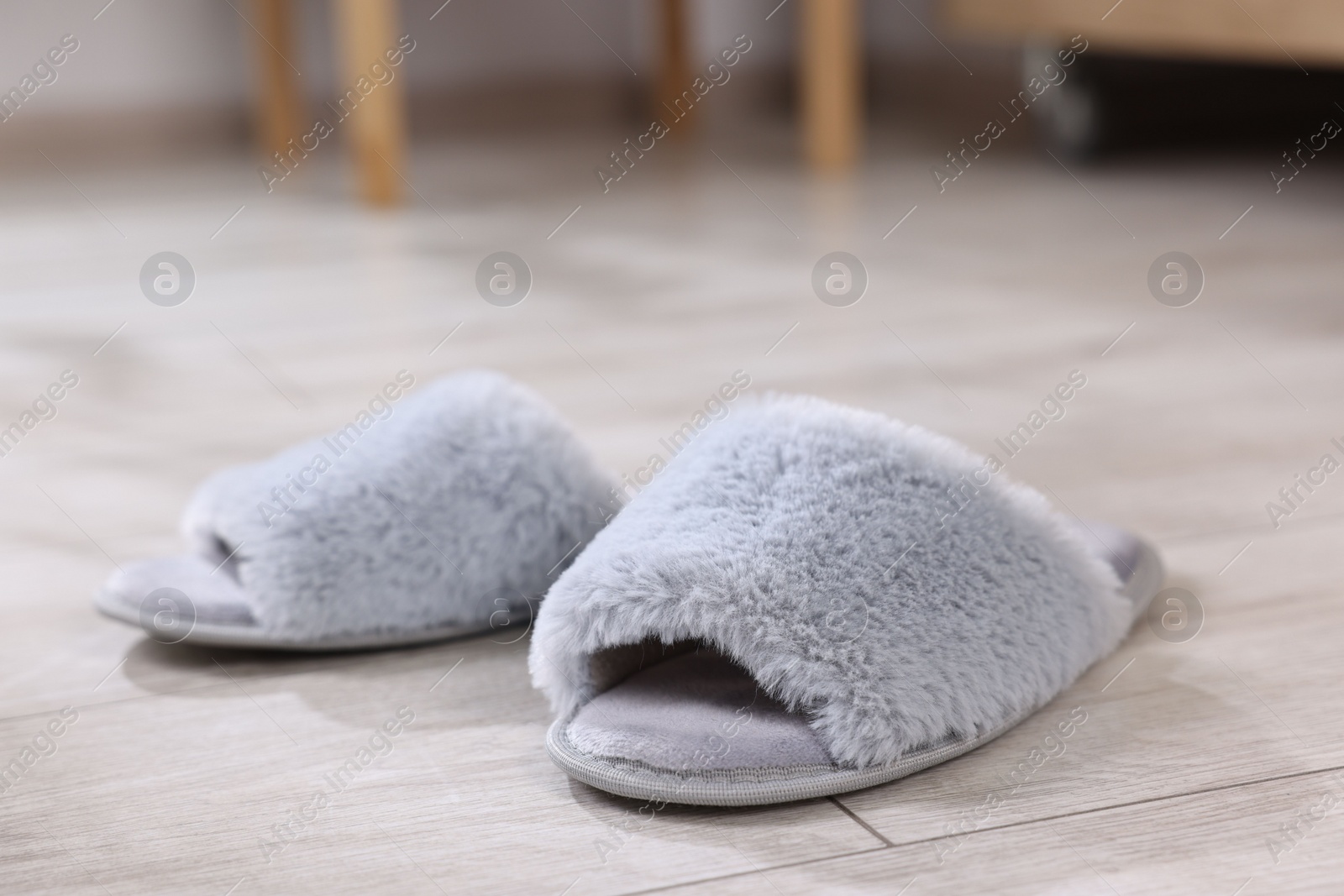 Photo of Grey soft slippers on light wooden floor at home, closeup