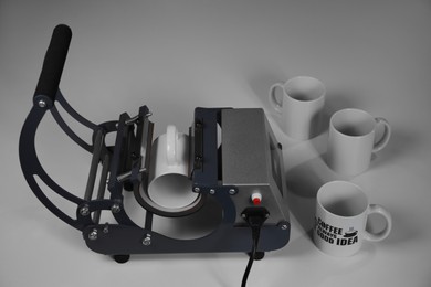 Photo of Printing logo. Heat press with cups on white table