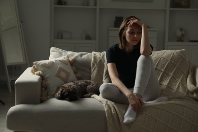 Sad young woman and her dog on sofa at home