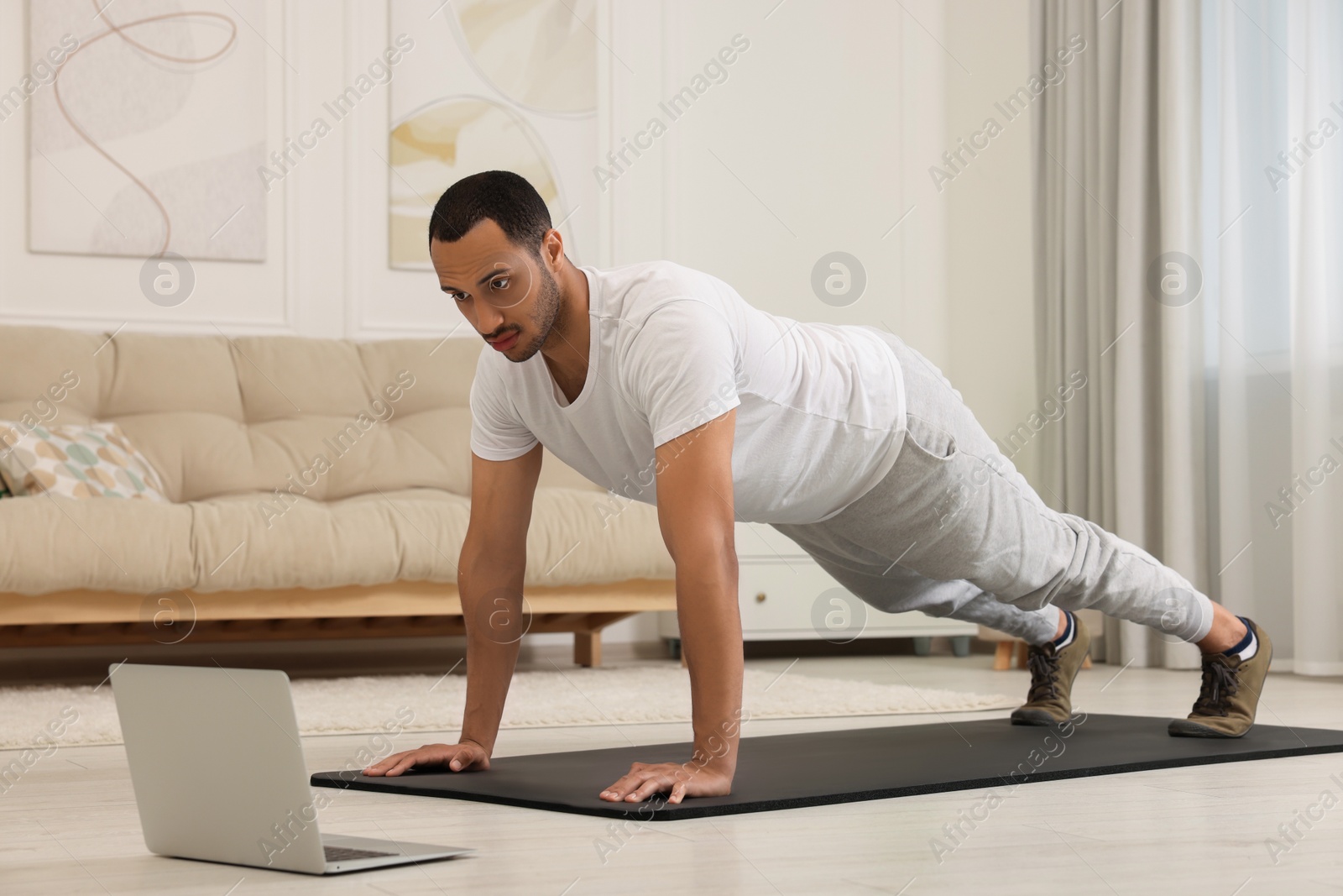 Photo of Man doing morning exercise on fitness mat near laptop at home