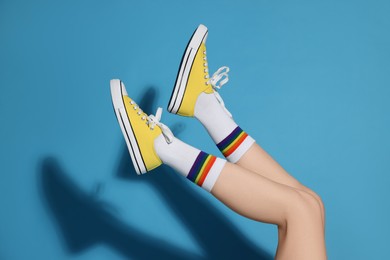 Woman posing in yellow classic old school sneakers on light blue background, closeup