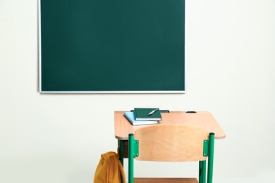 School desk with stationery and bag near chalkboard in classroom