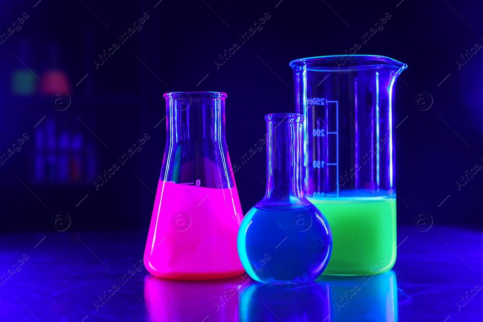 Photo of Laboratory glassware with luminous liquids on table against dark blue background