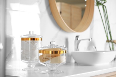 Jars with cotton pads and loofah sponges on countertop in bathroom