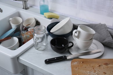 Photo of Many dirty utensils and dishware on countertop in messy kitchen