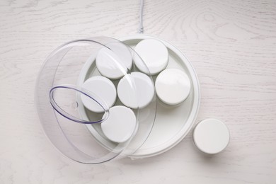 Modern yogurt maker with jars on white wooden table, flat lay