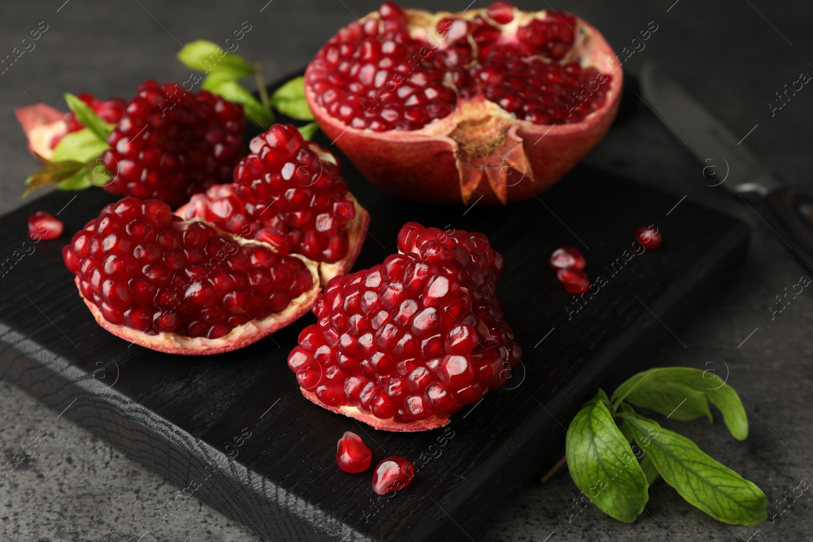 Photo of Cut fresh pomegranate, green leaves and knife on grey table, closeup