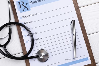Photo of Medical prescription form with empty fields, stethoscope and pen on white wooden table, flat lay