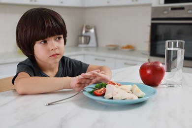 Photo of Cute little boy refusing to eat dinner in kitchen
