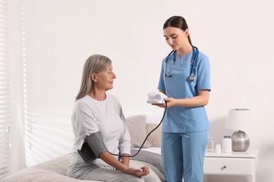 Young healthcare worker measuring senior woman's blood pressure indoors