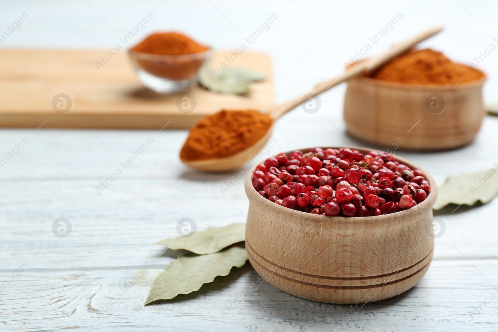 Photo of Bowl of red pepper corns and bay leaves on white wooden table, space for text