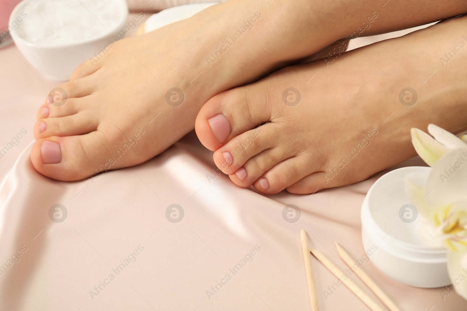 Photo of Woman with neat toenails after pedicure procedure on silk fabric, closeup