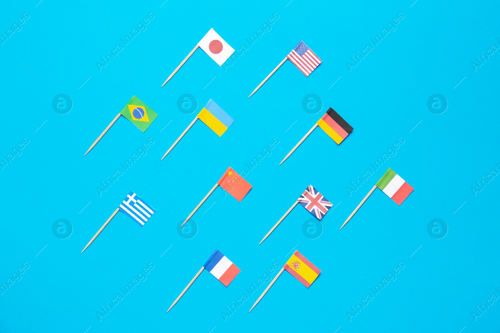 Photo of Many small paper flags of different countries on light blue background, flat lay