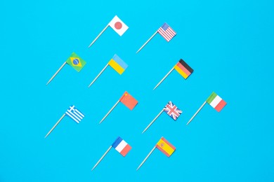 Photo of Many small paper flags of different countries on light blue background, flat lay