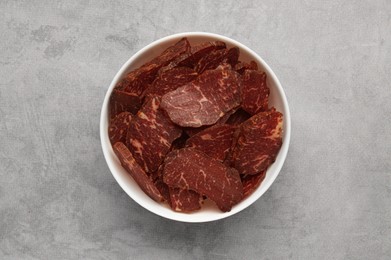 Photo of Delicious beef jerky in bowl on light gray table, top view