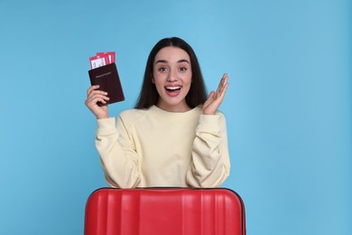 Happy woman with passport, tickets and suitcase on light blue background
