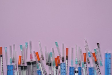 Disposable syringes with needles on violet background, flat lay. Space for text