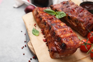 Photo of Tasty roasted pork ribs served with basil on grey table, closeup. Space for text