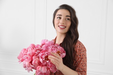 Beautiful young woman with bouquet of pink peonies near white wall