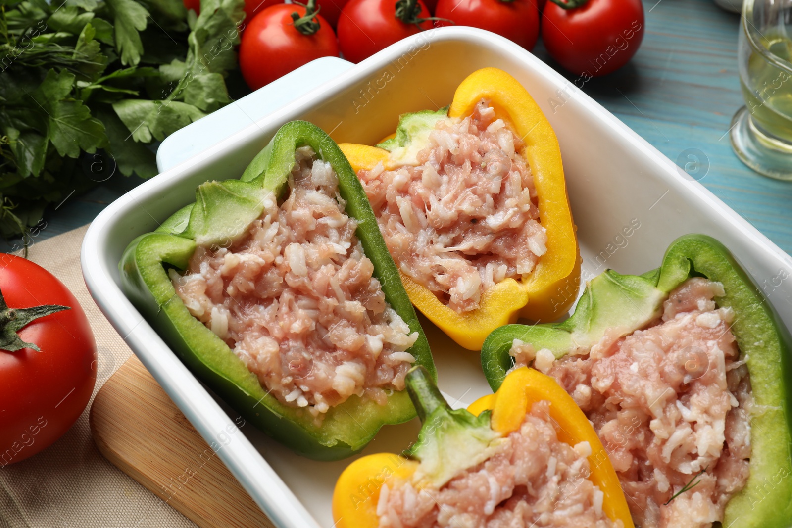 Photo of Raw stuffed peppers and ingredients on light blue wooden table, closeup