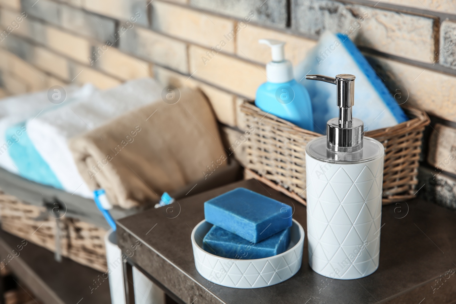 Photo of Dish with soap bars and bottle of shampoo on table near brick wall