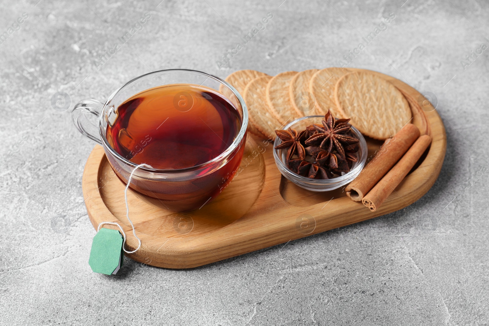 Photo of Tea bag in glass cup, anise stars, cinnamon sticks and cookies on light grey table