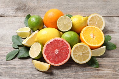 Different fresh citrus fruits and leaves on wooden table, closeup