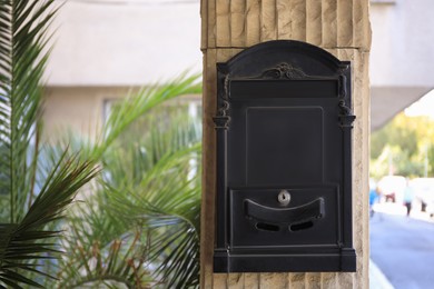 Photo of Black metal letter box on beige column outdoors, space for text