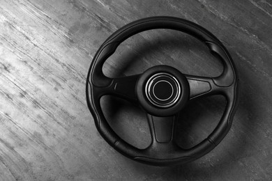 Photo of New black steering wheel on grey wooden table, top view. Space for text