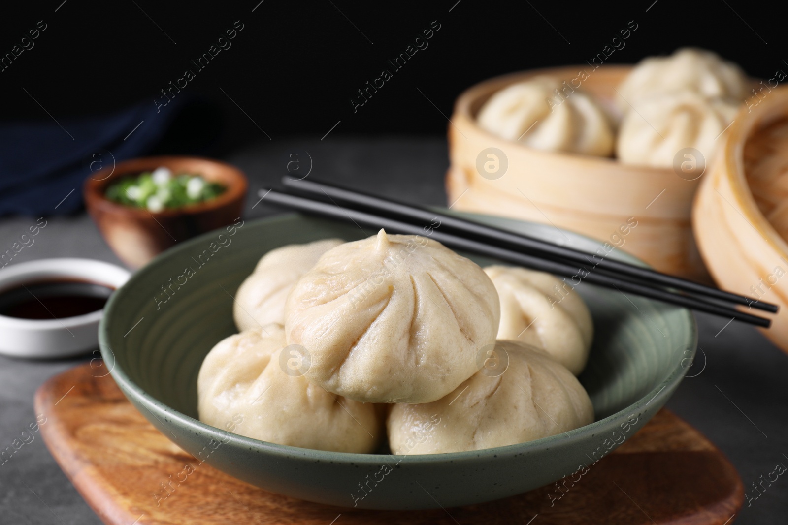 Photo of Delicious bao buns (baozi) in bowl and chopsticks on grey table, closeup