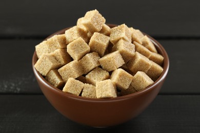 Photo of Brown sugar cubes in bowl on black wooden table, closeup