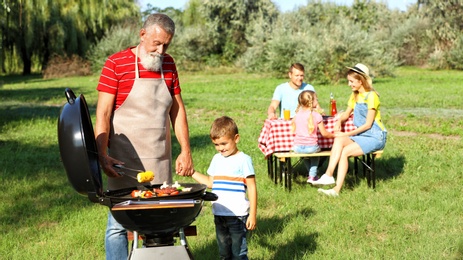 Photo of Grandfather with little boy at barbecue grill and their family in park