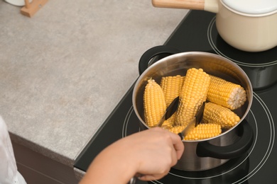 Photo of Woman preparing corn in stewpot on stove, closeup