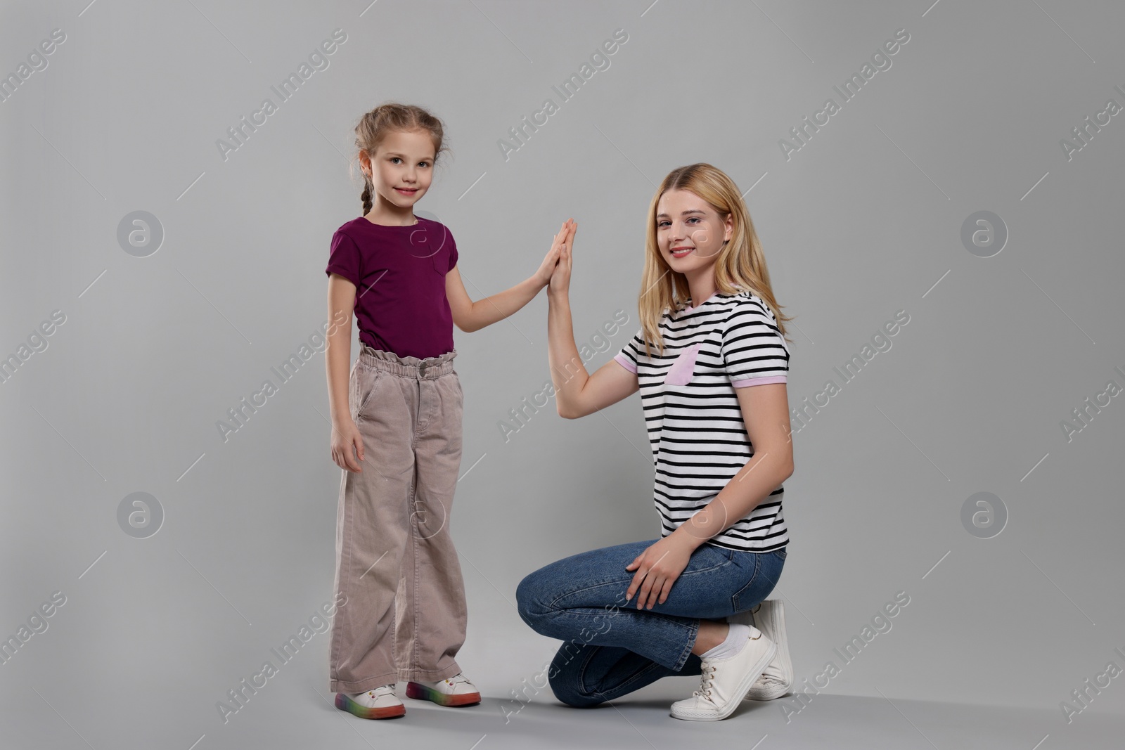 Photo of Mother and daughter giving high five on light grey background