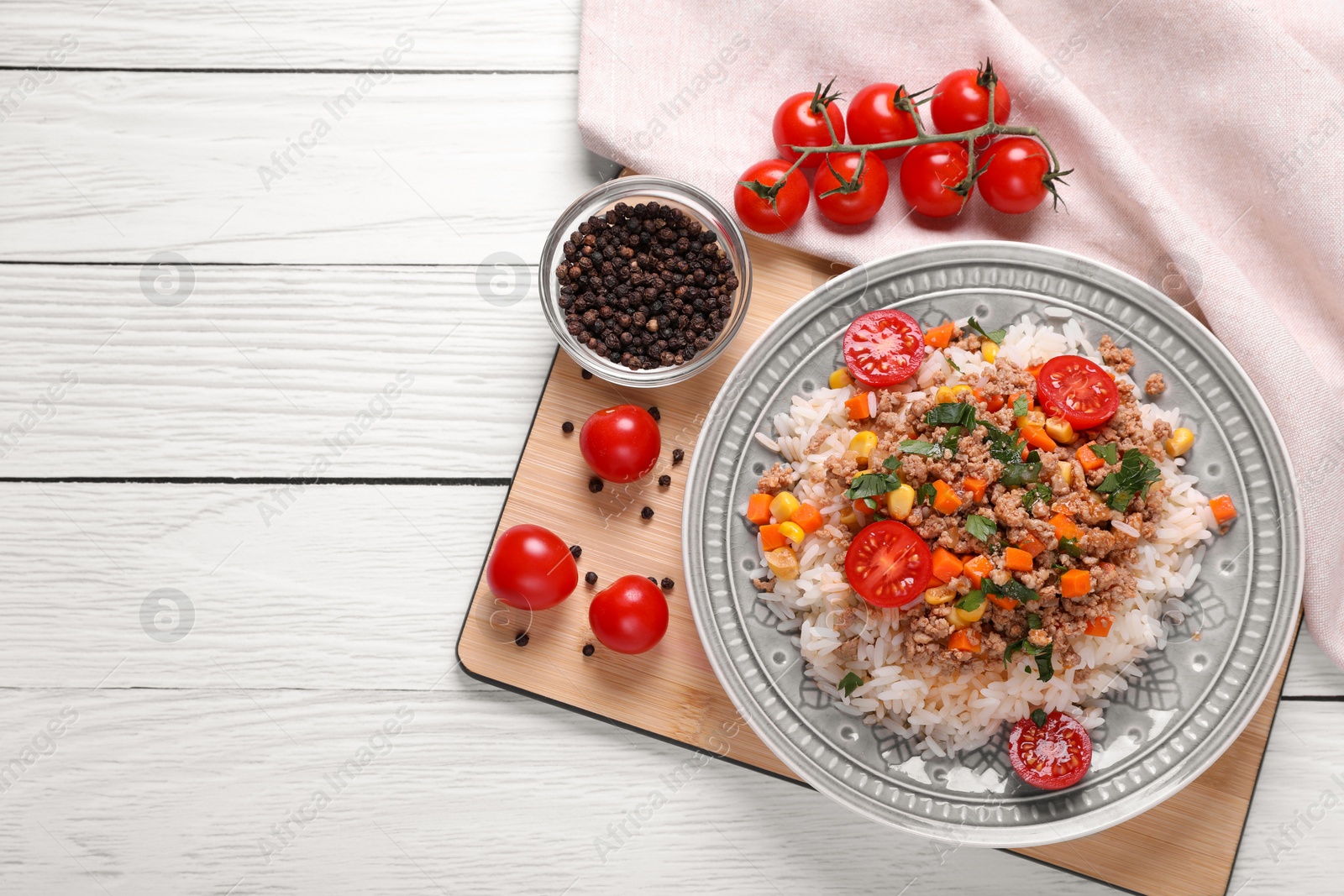 Photo of Tasty dish with fried minced meat, rice, carrot, tomatoes and corn on white wooden table, flat lay. Space for text