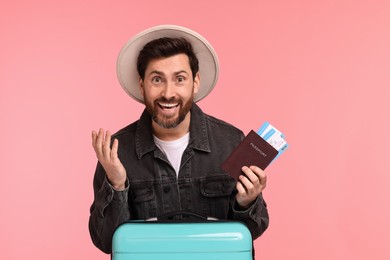 Smiling man with passport, tickets and suitcase on pink background