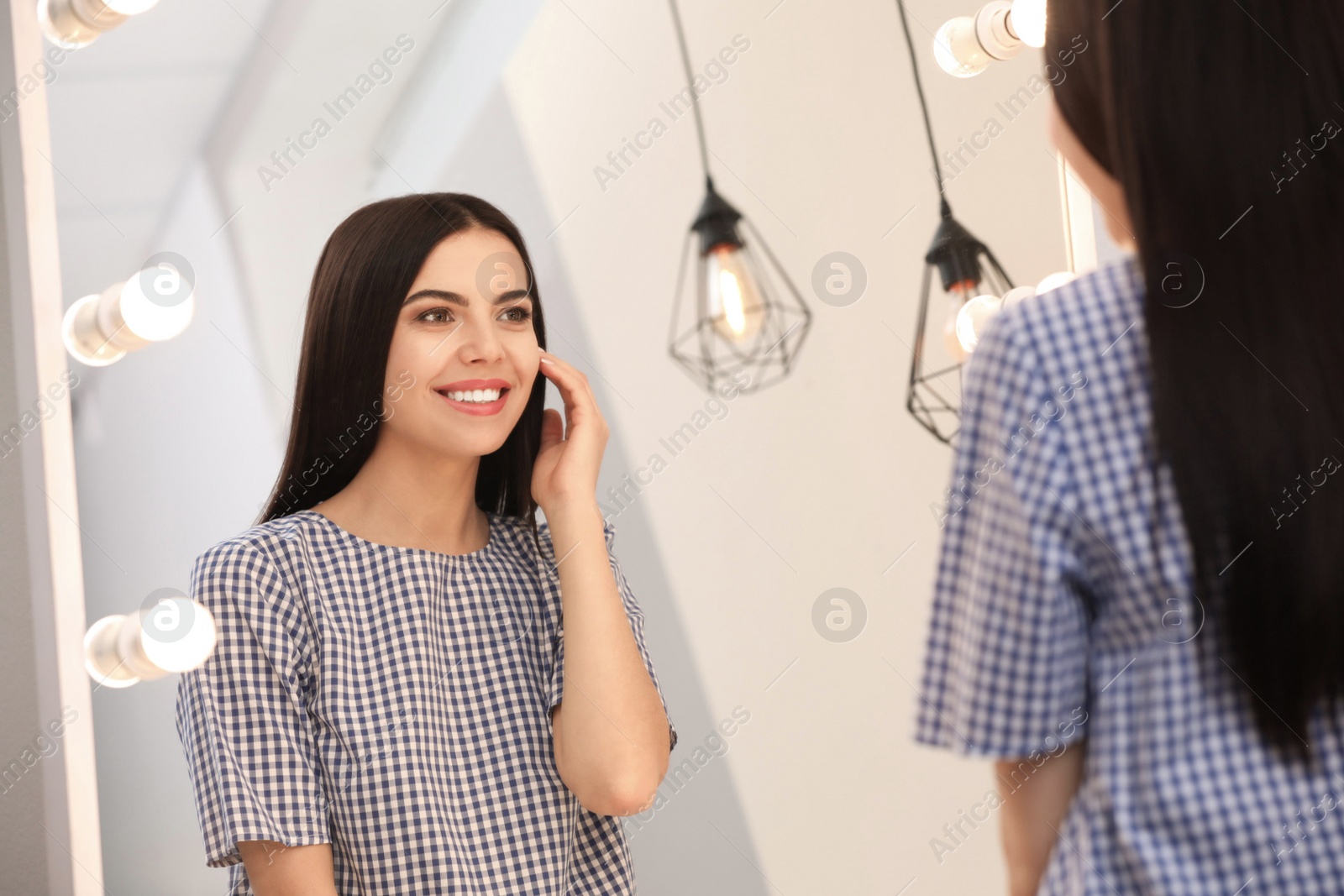 Photo of Young attractive woman looking at herself in stylish mirror at home