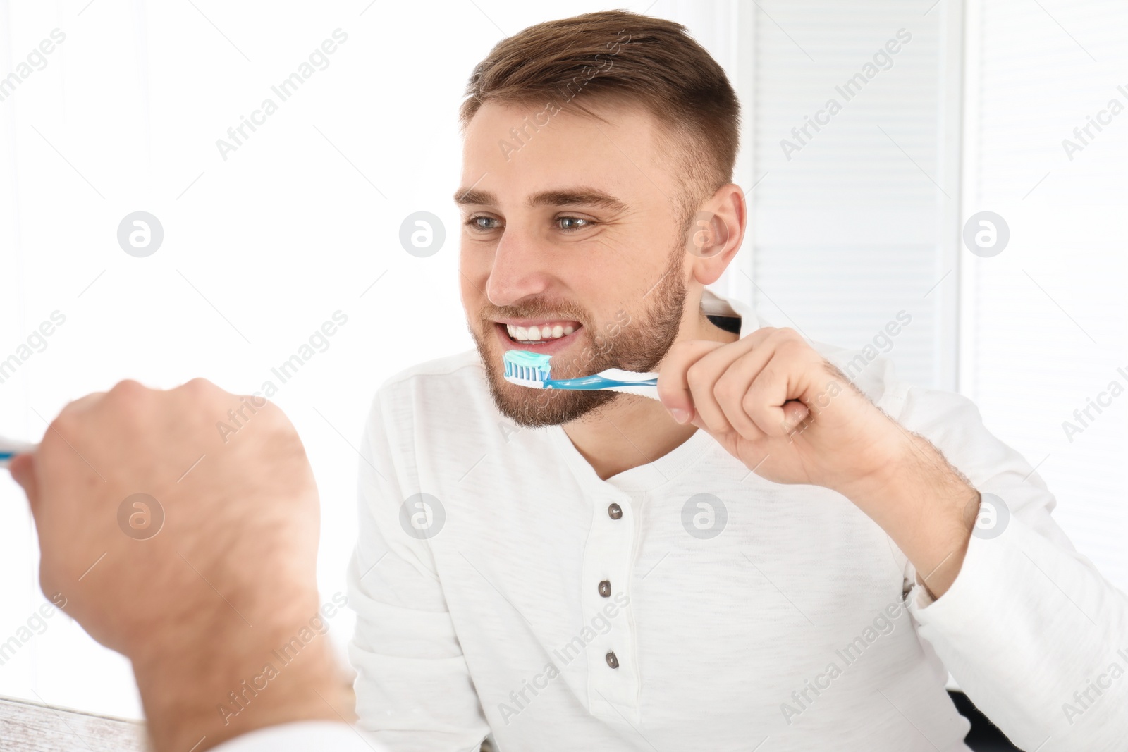 Photo of Young man cleaning teeth against mirror in bathroom