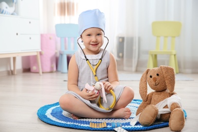 Cute child imagining herself as doctor while playing with stethoscope and toy bunny at home