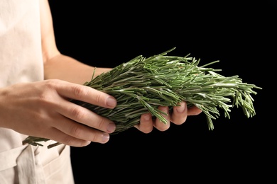 Woman holding fresh rosemary twigs on black background