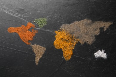 World map of different spices on dark textured table, flat lay