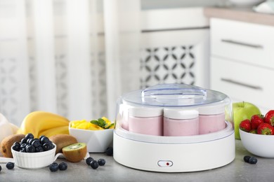 Yogurt maker with jars and different fruits on light grey table in kitchen