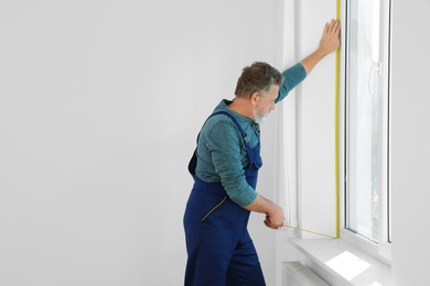 Photo of Service man measuring window for installation indoors. Space for text