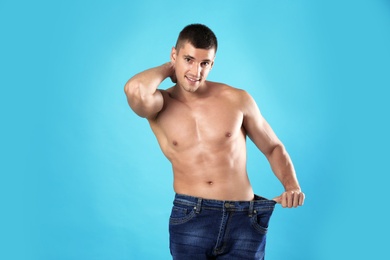 Young man with slim body in old big size jeans on light blue background, space for text