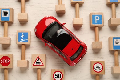 Photo of Many different miniature road signs and car on white wooden table, flat lay. Driving school